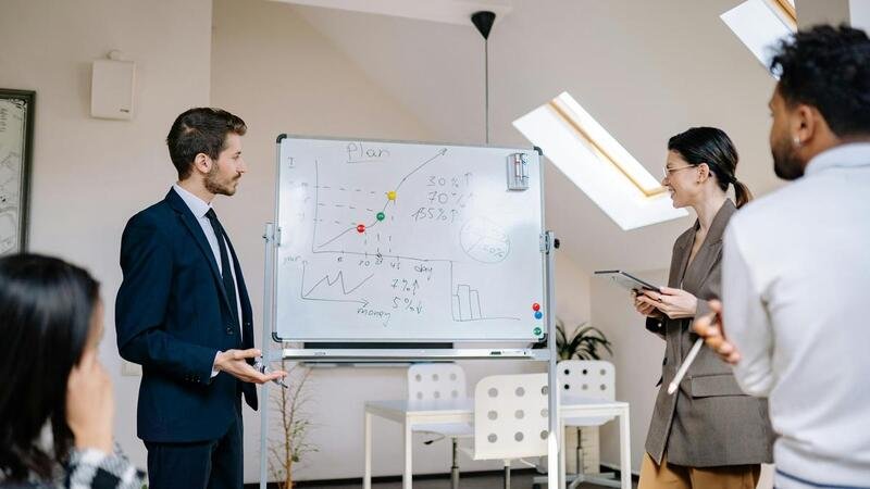 Colegas colaborando em uma reunião de negócios, analisando gráficos em um quadro branco